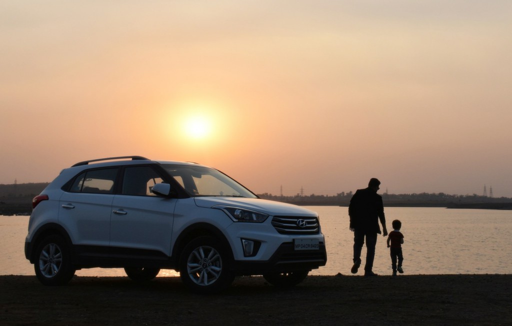 Photograph of a man and child next to a Hyundai family car watching the sunset
